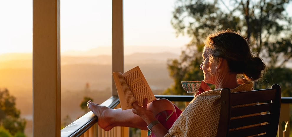 A woman reading a book on a balcony, at sunset