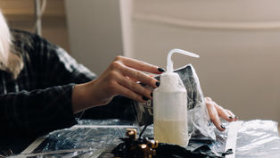 Gloved hands disinfecting a plastic-wrapped tattoo workstation
