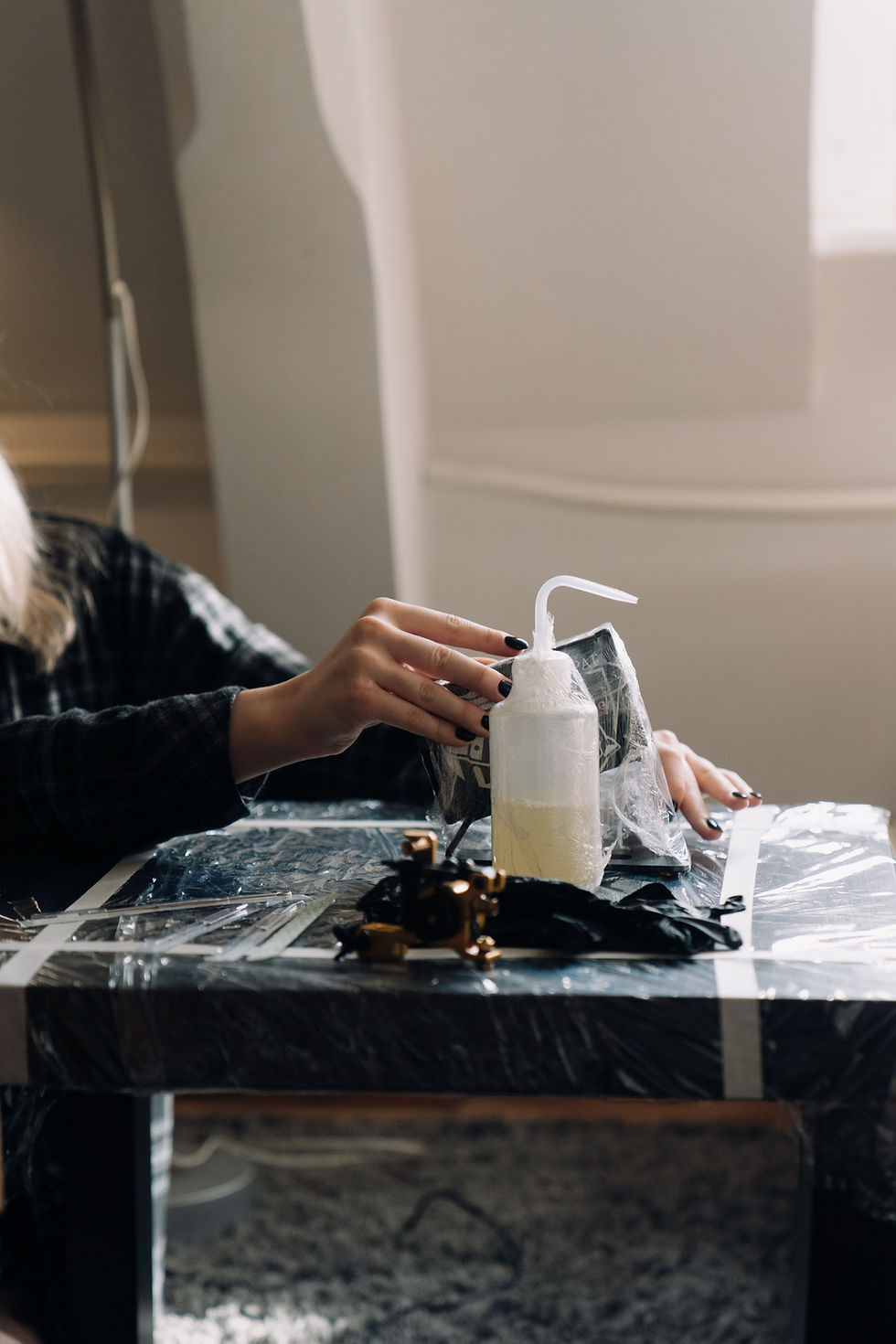Gloved hands disinfecting a plastic-wrapped tattoo workstation