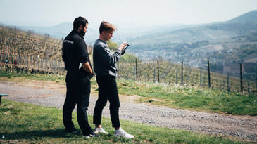 Regisseur und Kameramann diskutieren eine Szene vor einer weiten Weinberglandschaft.
