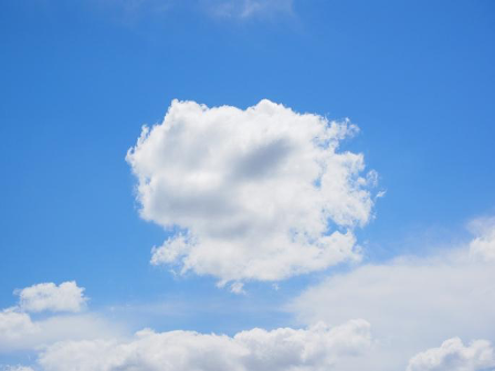 Fluffy white clouds drift across a bright blue sky, evoking a calm, serene mood.