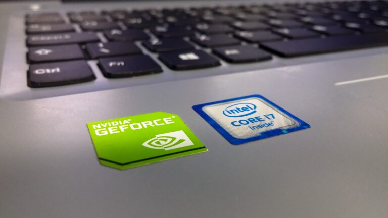 Close-up of a laptop with NVIDIA GeForce and Intel Core i7 stickers on the silver surface, with a keyboard in the blurred background.