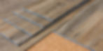 Wooden flooring planks being assembled, lying on a cork sheet. Natural wood grain and tones visible, suggesting construction or renovation.
