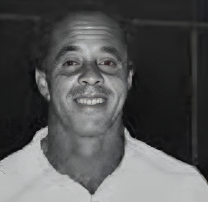 Monochrome portrait of a smiling Lloyd 'Lindy' Delapenha in a white shirt.