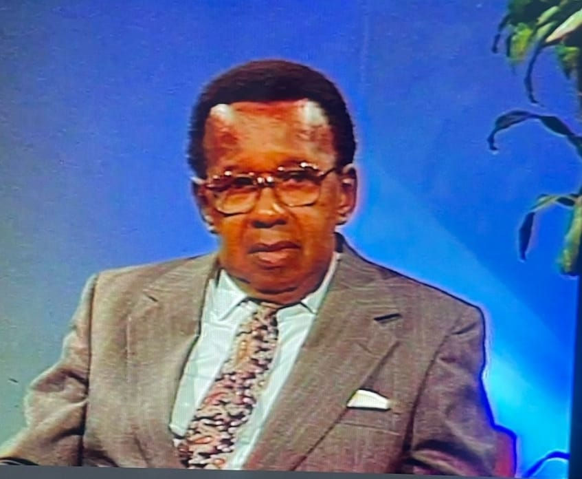 Wycliffe Bennett in a gray suit with a patterned tie sits against a blue background.