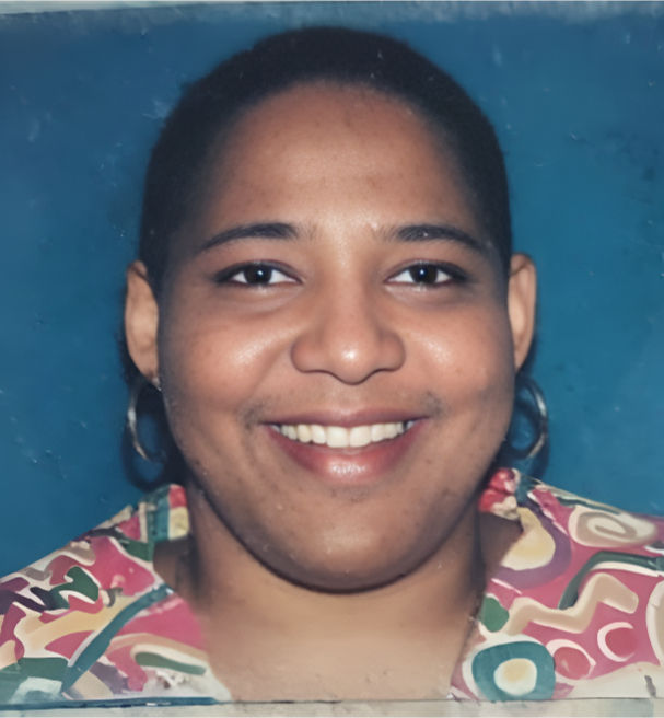 A smiling headshot of Gillian Haughton wearing a colorful patterned shirt against a blue background.