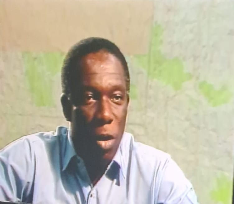 Harold 'Harry' Nixon, seated and wearing a blue shirt, with a topographical map in the background.