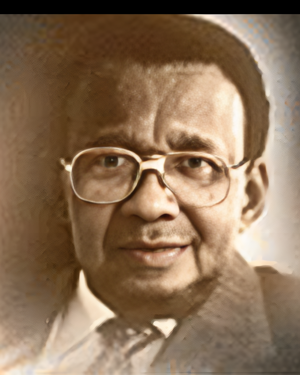 Wycliffe Bennett, wearing glasses and a suit, smiles in a close-up portrait