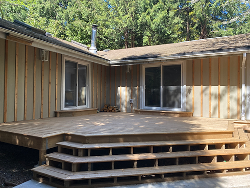 a new wood deck off a home. The deck is triangular and provides outdoor access to two sliding glass doors. 
