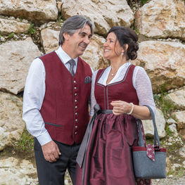 Paar in weinrotem Festtagsdirndl und Trachtenweste vor Felswand