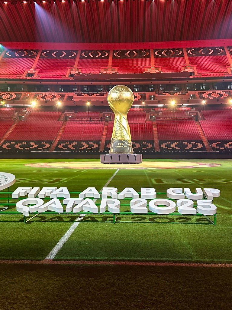 Trophée de 8m de haut dorée au milieu d'un stade de football.
