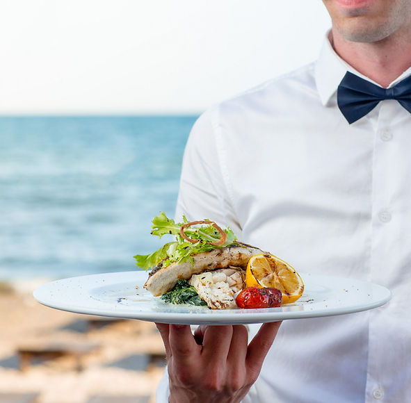 waiter-holding-grilled-fish-with-lemon-tomato-creamy-herbs-at-the-seaside-restaurant.jpg
