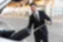 uomo-d-affari-felice-in-abbigliamento-formale-che-mette-la-valigia-nel-bagagliaio-dell-aut