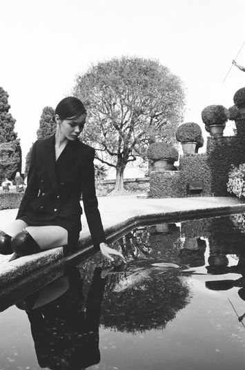 fashion analog portrait of a beautiful brunette girl sitting near the fountain with fish wearing Emilio Pucci blazer