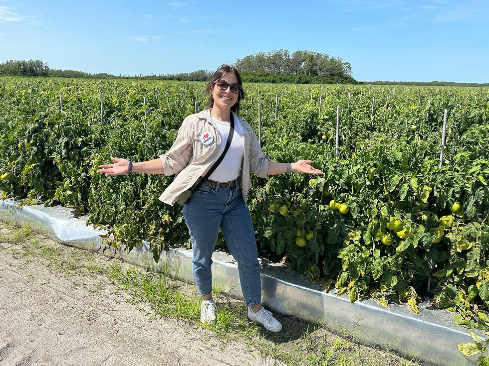 Diana, a Latina woman standing with arms open in a field of green tomatoes