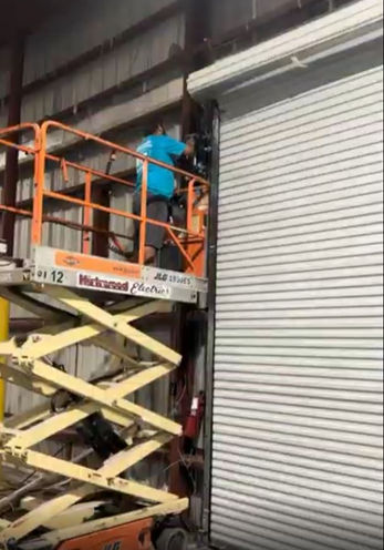 Commercial roll-up garage door installation being completed with a scissor lift