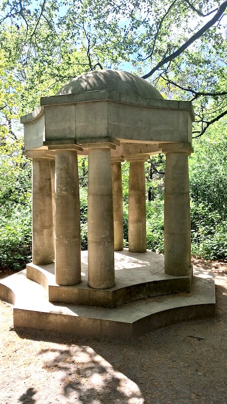 A greek looking stone temple set in a bright woodland