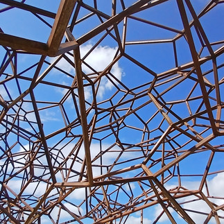 The sky shines bright blue above the rusted intricate steel sculpture