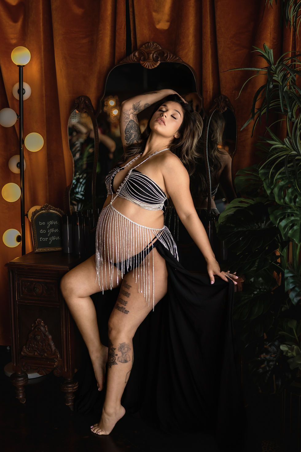 Pregnant woman poses confidently in black and white outfit, amid orange curtains and plants. Text reads "be you, do you, for you.". Maternity Boudoir Session done at Dark Luxe Studio in Crowley Texas taken by Precious Gems Photography.