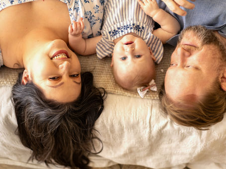 Family Portrait DescriptionA beautiful family of three is captured in a unique pose, laying on a bed upside down. The scene features:The baby and mom looking directly at the cameraDad gazing affectionately at his daughterStudio InformationThis heartwarming moment was photographed at White Magnolia Studio in Saginaw, Texas, by Precious Gems Photography.