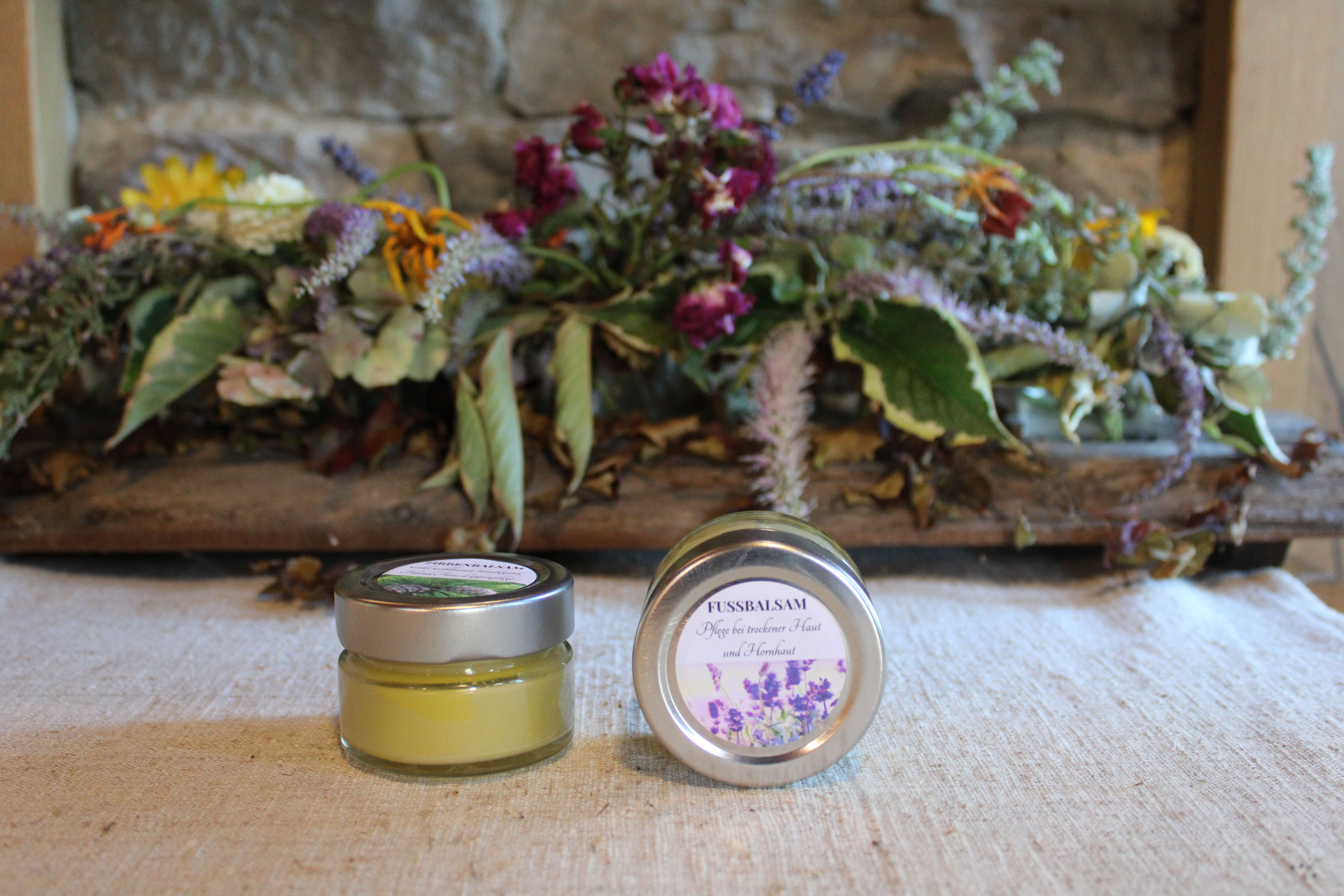 Zwei kleine Dosen Lavendelsalbe vor Blumenarrangement