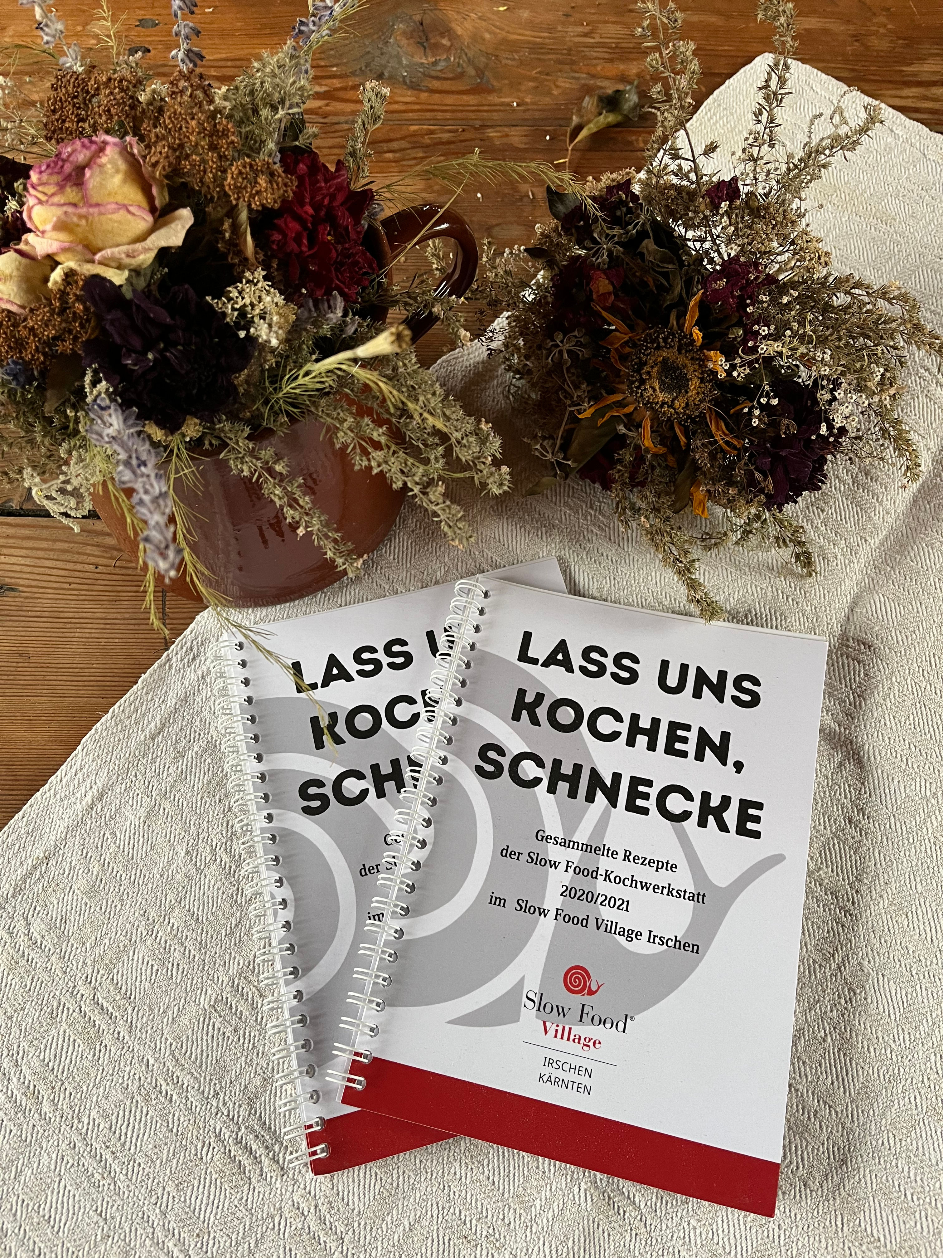 Zwei Kochbücher, "Lass uns kochen, Schnecke", liegen neben Trockenblumen.