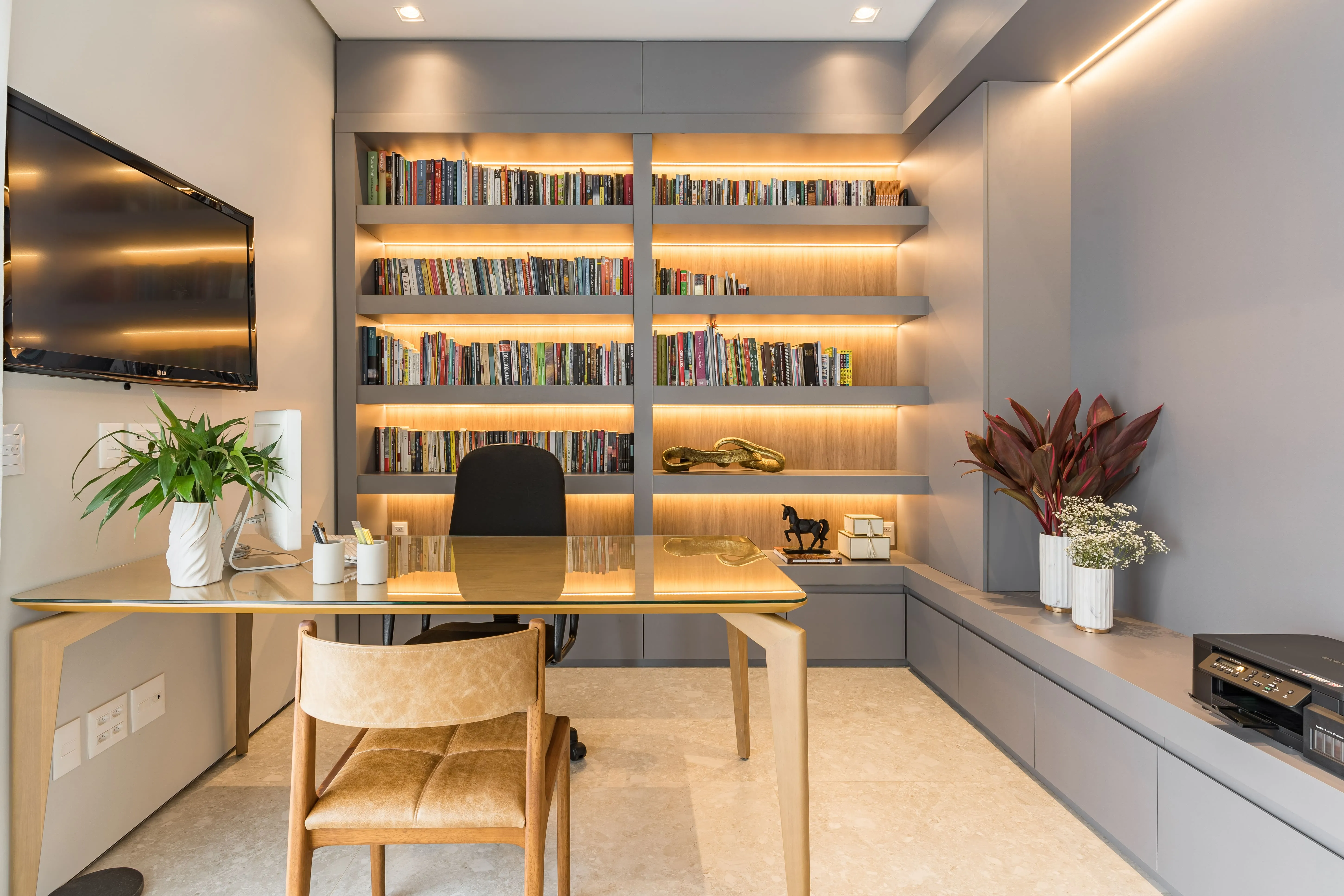 Home office elegante com biblioteca iluminada, mesa de madeira e marcenaria planejada que integra trabalho e leitura.