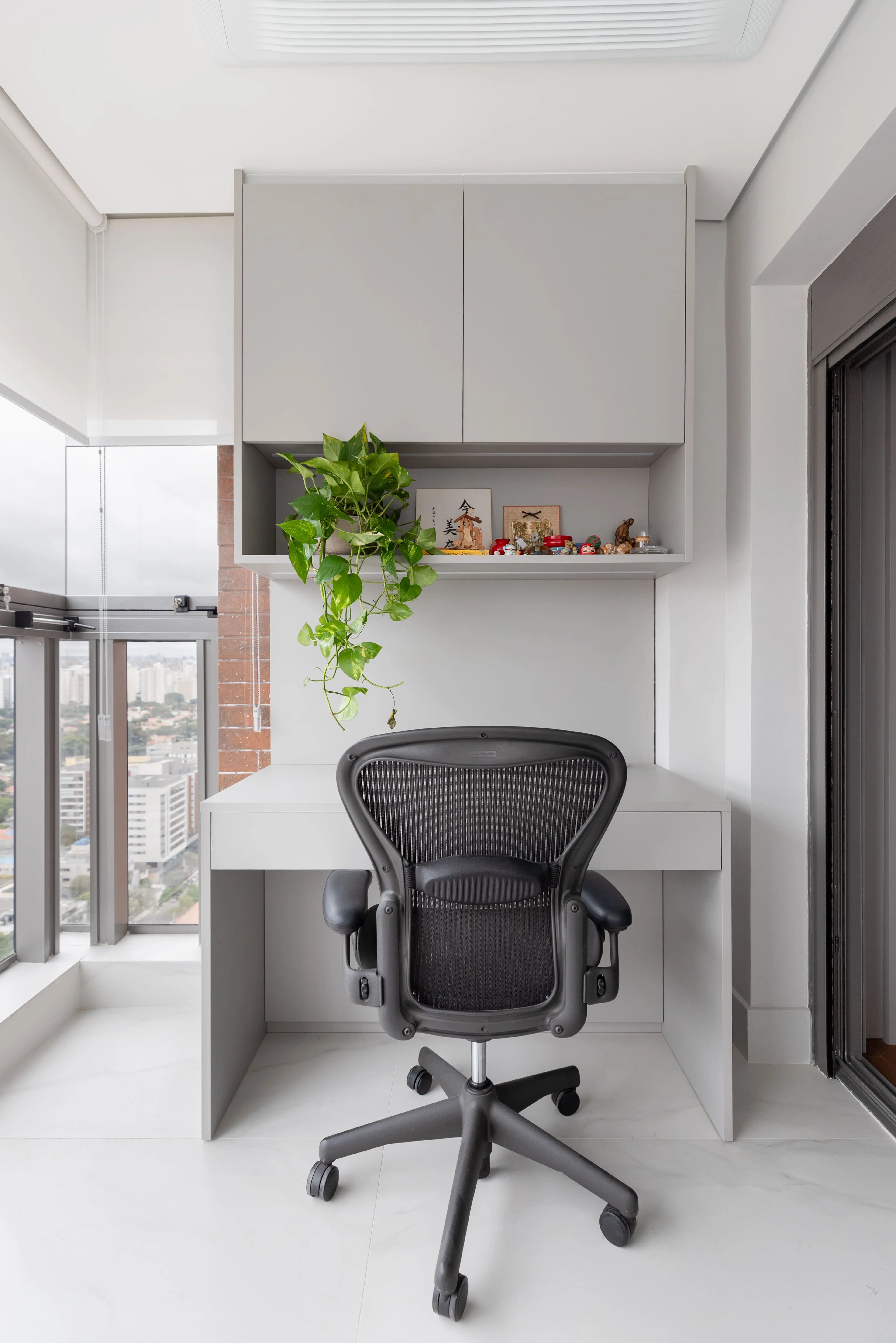 Escritório em casa com cadeira ergonômica, prateleira minimalista e planta pendente que traz elementos naturais para o espaço de trabalho.
