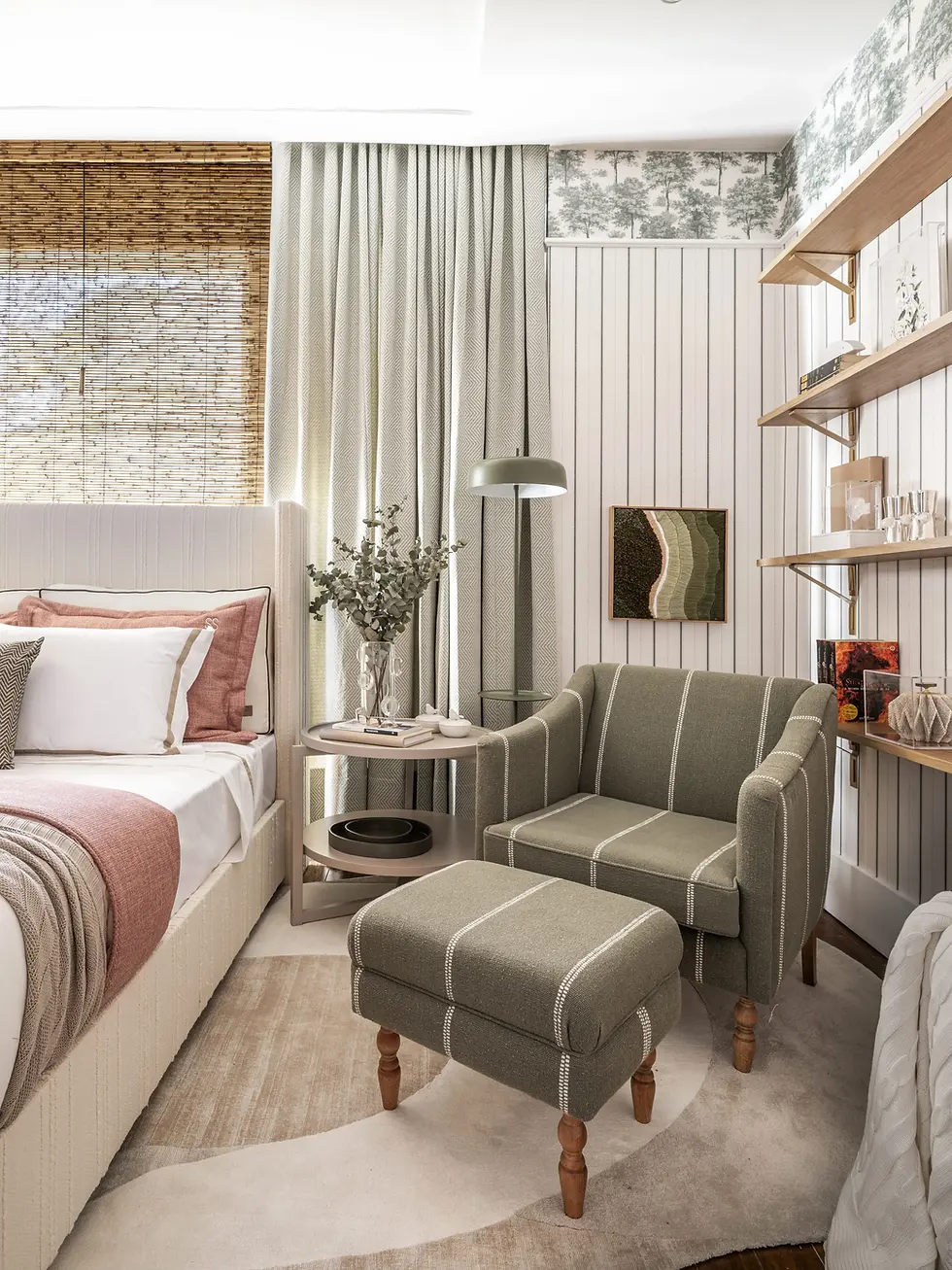 Quarto aconchegante com poltrona verde listrada, cama bege com almofadas rosa, cortinas brancas, e prateleiras de madeira decoradas.
