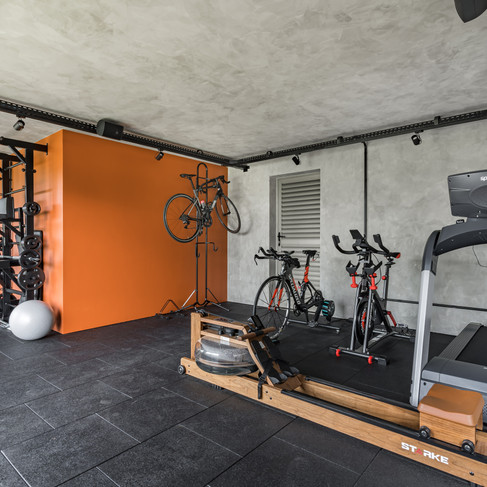 academia em casa, com equipamentos modernos, iluminação de estúdio, ventilação aberta e parede laranja.