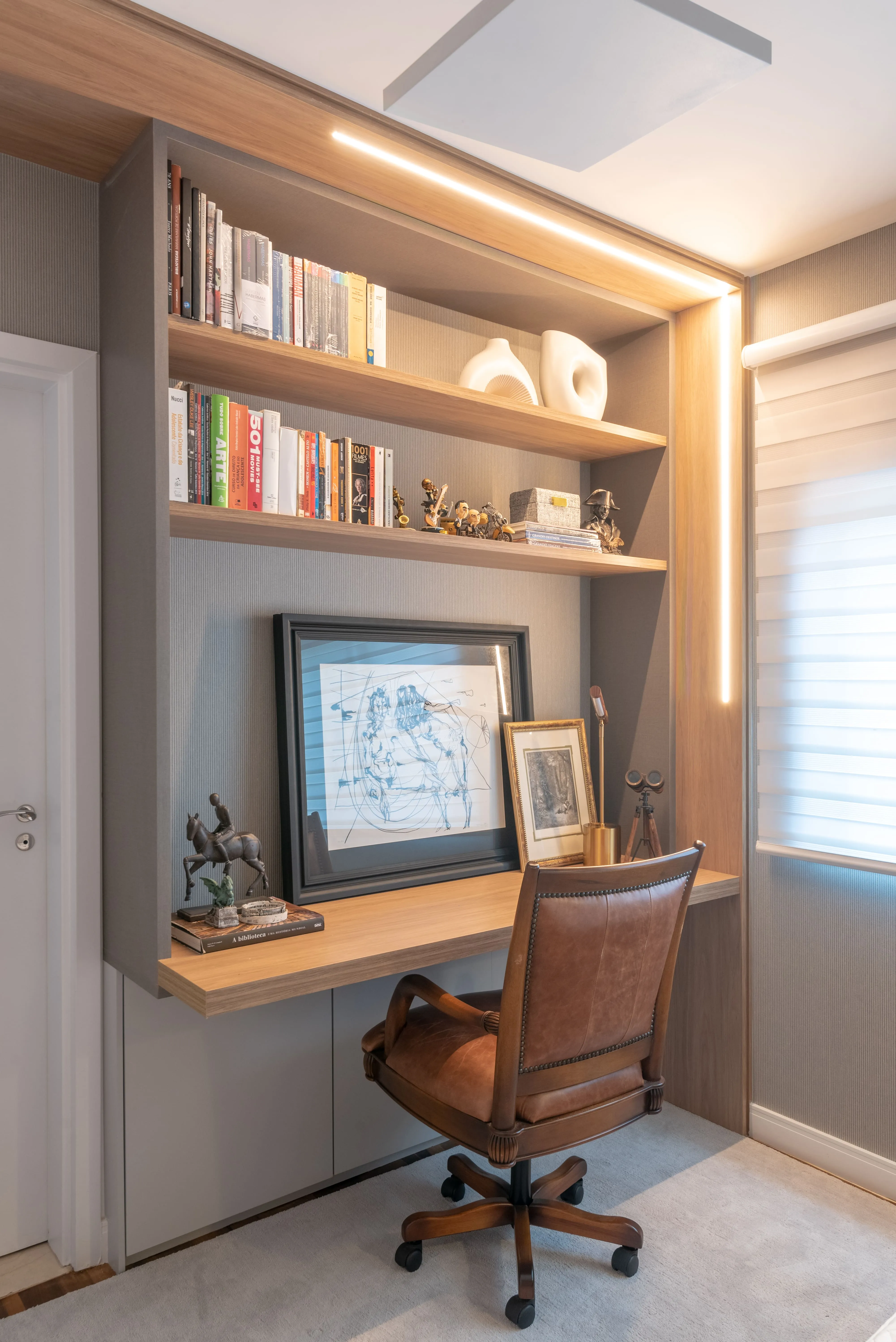 Cantinho de home office com prateleiras de madeira iluminadas, livros decorativos e mesa de trabalho integrada à marcenaria.
