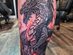 Black and grey dragon tattoo with red fire and a castle on a client's lower leg by Black Brew Tattoo, Abbotsford