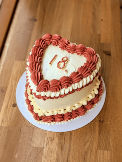 Heart-shaped birthday cake with red and vanilla buttercream piping and a piped “18” on top in a retro style.