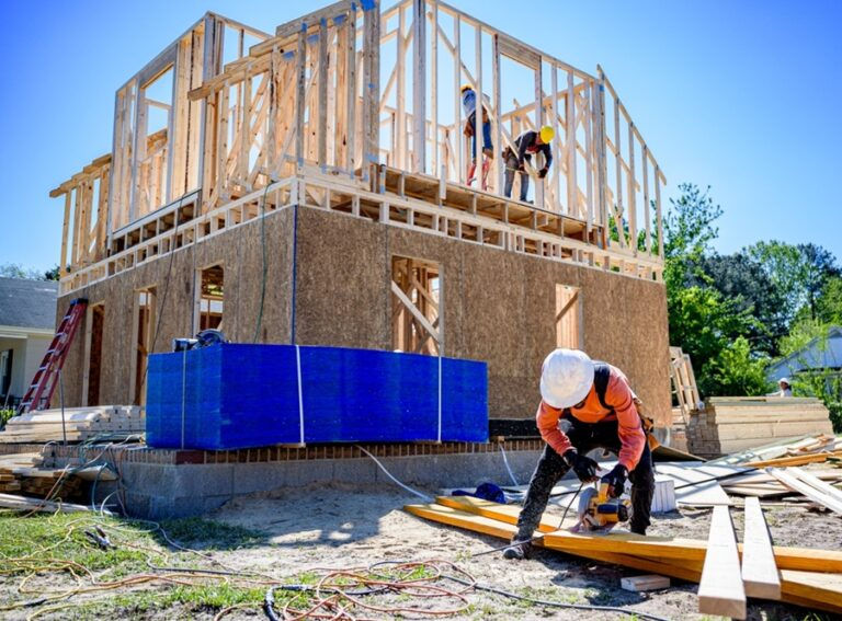Construction workers building a new home frame on a residential lot, representing post-wildfire rebuilding and real estate development in high-risk zones like Malibu
