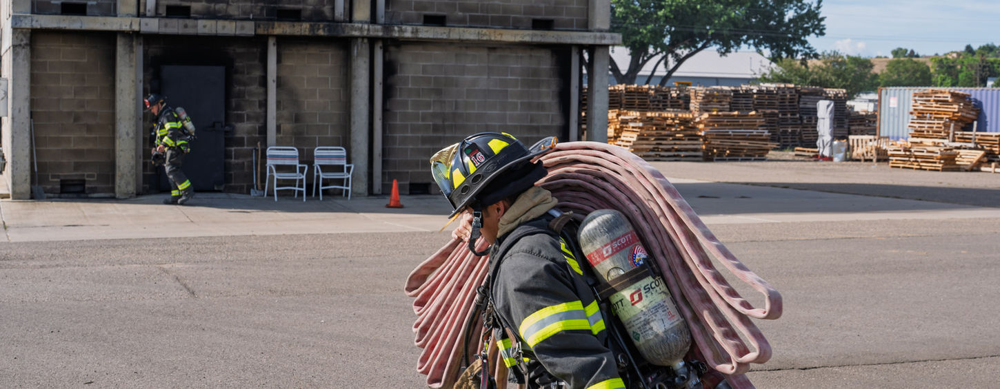 Wellington Firefighter carrying hose in a training scenario.