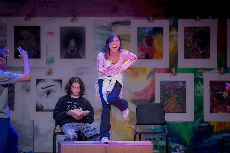 Actress sings fun song about fashion while standing on stage cubes. Actor dances to music while another actor sits reading.