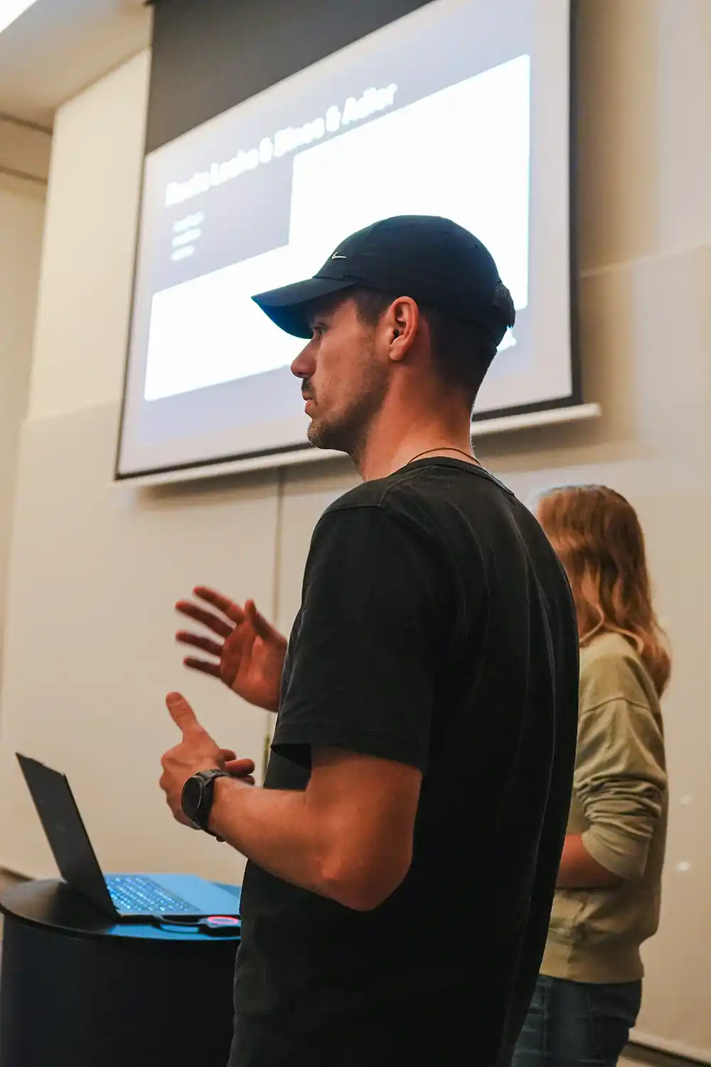 Nahaufnahme von Lukas Löer mit Cap und Sportuhr vor einer Präsentationsleinwand im 808 Scyence Trainingcamp auf Mallorca