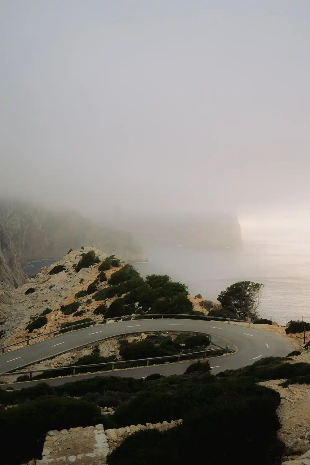 Kurvenreiche Küstenstraße am Cap de Formentor auf Mallorca bei Nebel und Meerblick. 