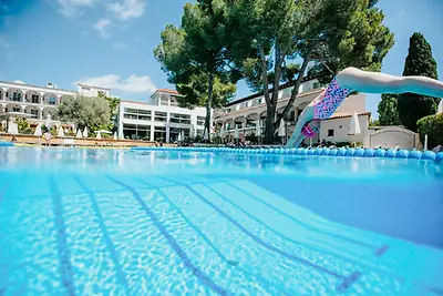 Eine Schwimmerin mit Badekappe und Schwimmbrille springt kopfüber in den menschenleeren Hotelpool des Fergus Club Font de Sa Cala