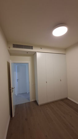 חדר שינה מחודש עם פרקט עץ חם, ארון קיר לבן ותאורה עגולה מודרנית, שיקום דירה לאחר נזקי מלחמה למשפחת ווידמן בנווה גן פתח תקווה | מעוז שפי קבלן שיפוצים רשום 35728