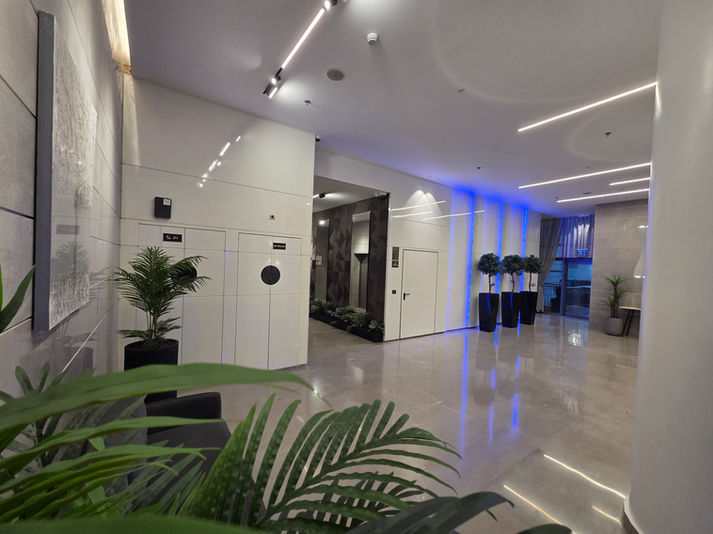 שיפוץ לובי בניין מגורים — תאורת LED כחולה אמביינט בין עמודי קיר, חיפוי לבן גלוסי, ריצוף שיש פוליש ועצי נוי מעוצבים | מעוז שפי קבלן שיפוצים ובנייה רשום, מרכז הארץ