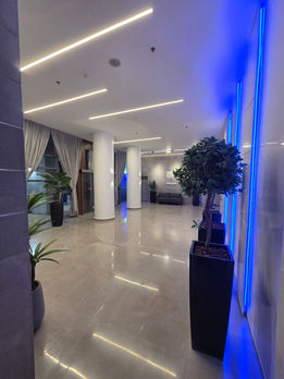לובי בניין מגורים לאחר שיפוץ קומפלט — רצועות LED כחולה אנכיות, עמודים עגולים לבנים, ריצוף שיש פוליש נרחב ועצי נוי מעוצבים | מעוז שפי קבלן שיפוצים ובנייה רשום, מרכז הארץ