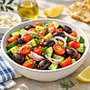 Colorful Greek vegetable salad with tomatoes, cucumbers, Kalamata olives, red onion, and fresh herbs in a bowl.