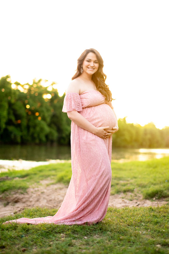 A pregnant woman in a pink dress holds her belly during a maternity session in Bastrop, Texas.