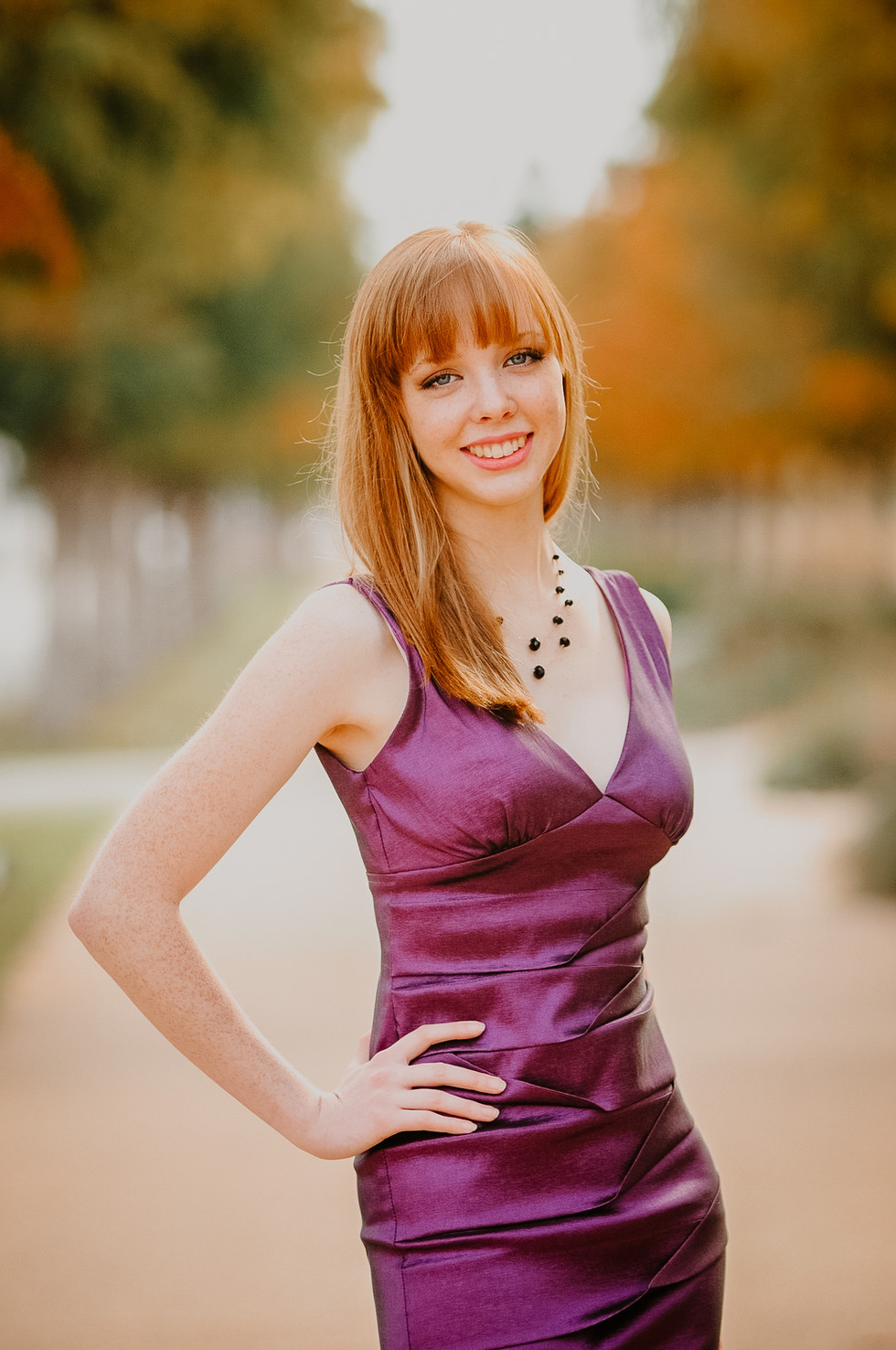 A Red haired beautiful senior in the Austin area poses in a purple dress.