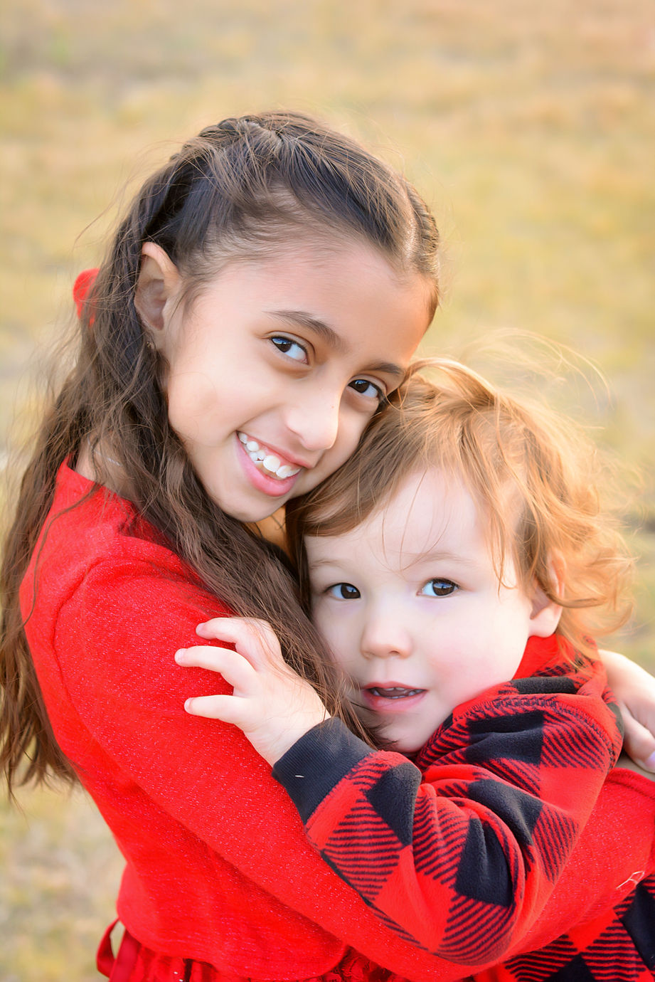 Two cousins wearing red hug each other for Christmas photos.