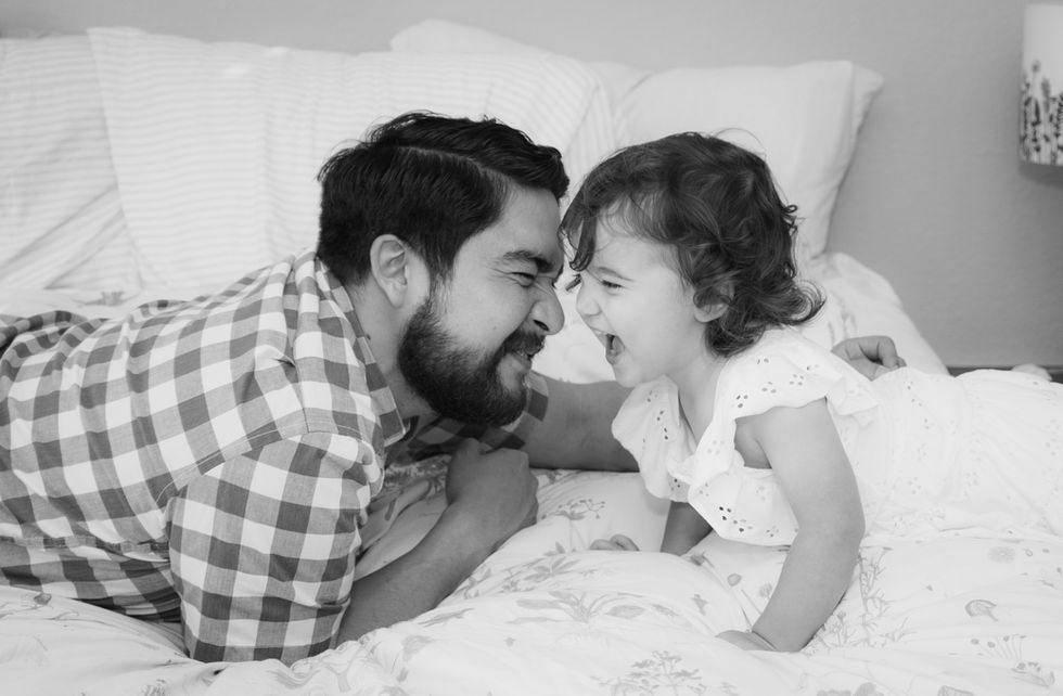 A dad and daughter laugh as they almost touch noses in a black and white photo.