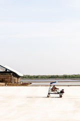 A worker riding a machine on a salt farm with a shed in the background