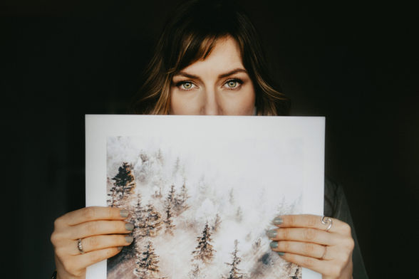 Frau hält ein Kunstprint mit winterlicher Waldszene vor ihr Gesicht.