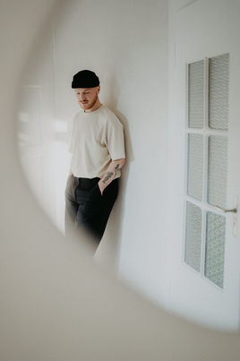 Person mit Mütze steht lässig im Flur, fotografiert durch runden Spiegel.
